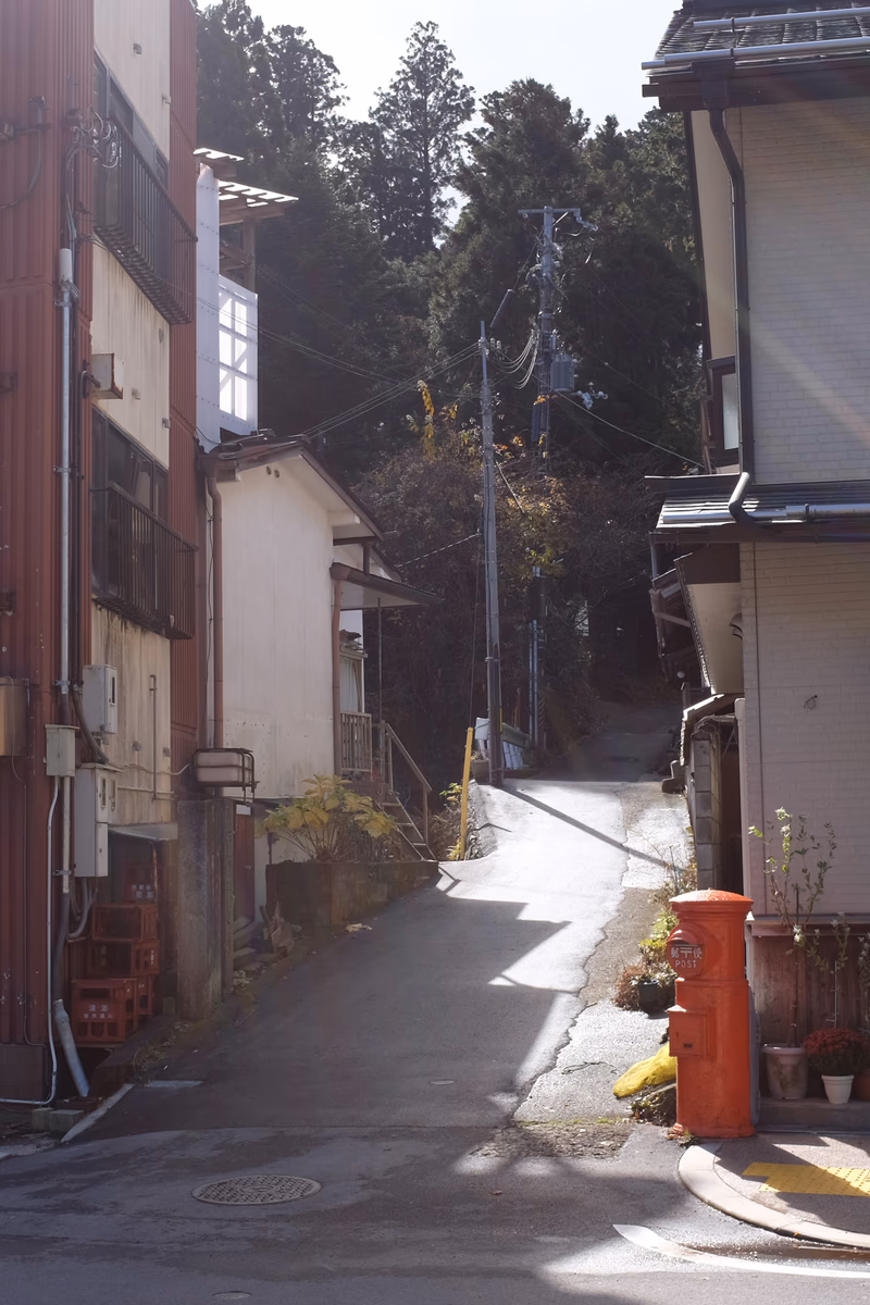A quiet street in a residential area with a sloped path leading up to a hill, surrounded by trees and buildings.