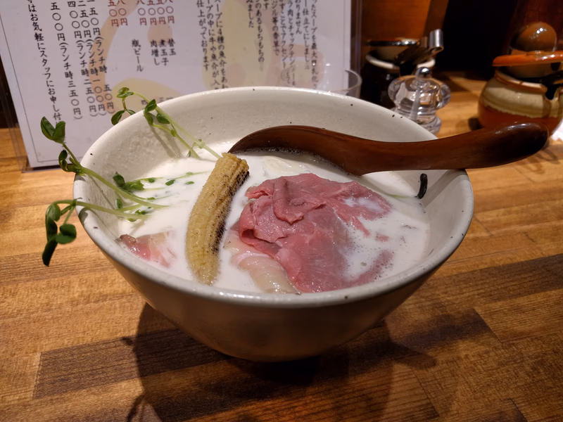 A bowl of soup with ingredients like meat, pickles, and a wooden spoon