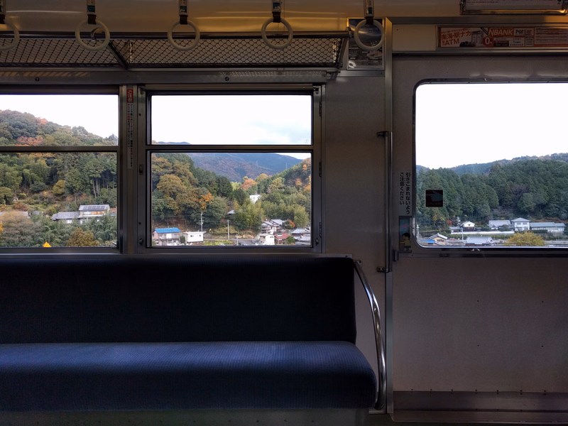A view from a train window shows a mountainous landscape with scattered houses, and the interior features blue seating.