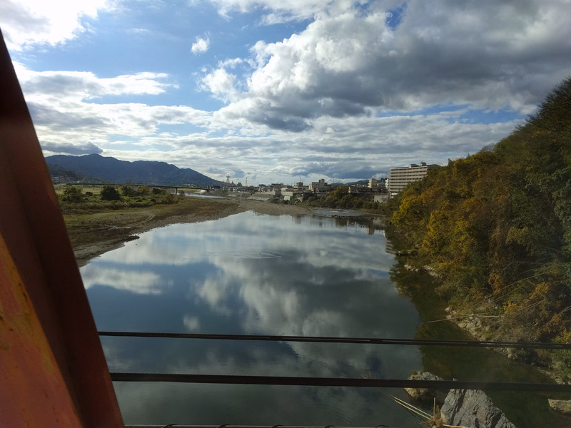 A wide river reflects a dramatic sky filled with white and gray clouds, bordered by dense trees on the right bank.