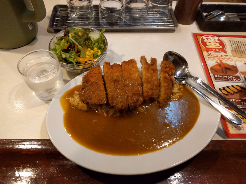 A plate of katsu curry with fried cutlets covered in brown curry sauce, served with a side salad.