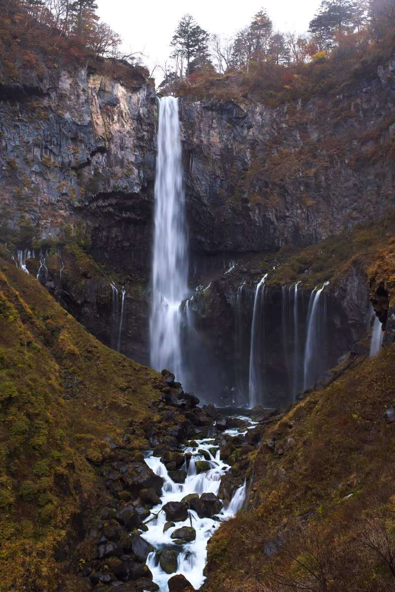 A tall, powerful waterfall cascades down a dark, moss-covered cliff face surrounded by dense forest.