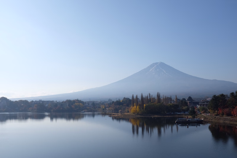 A large, snow-capped mountain reflects in a calm lake under a clear blue sky.