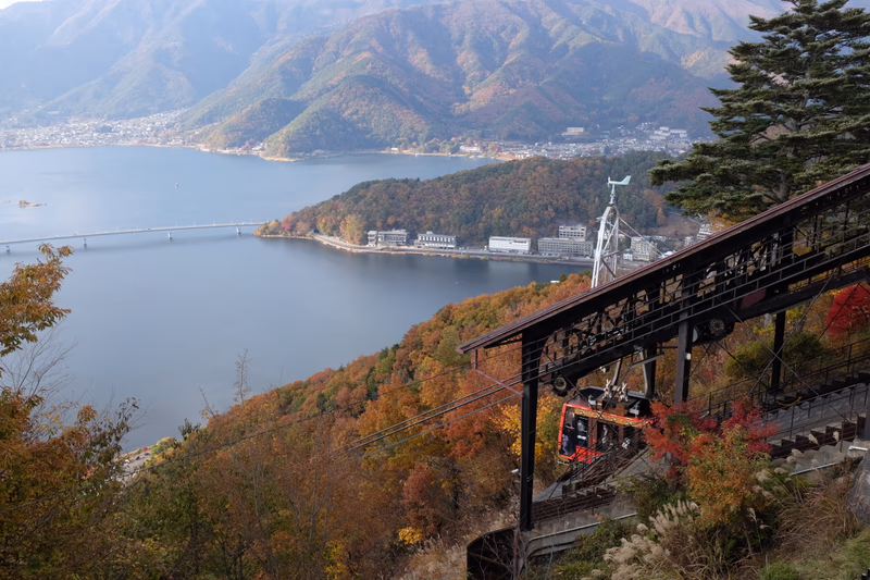 A cable car in the mountains near a lake, with a town in the background.