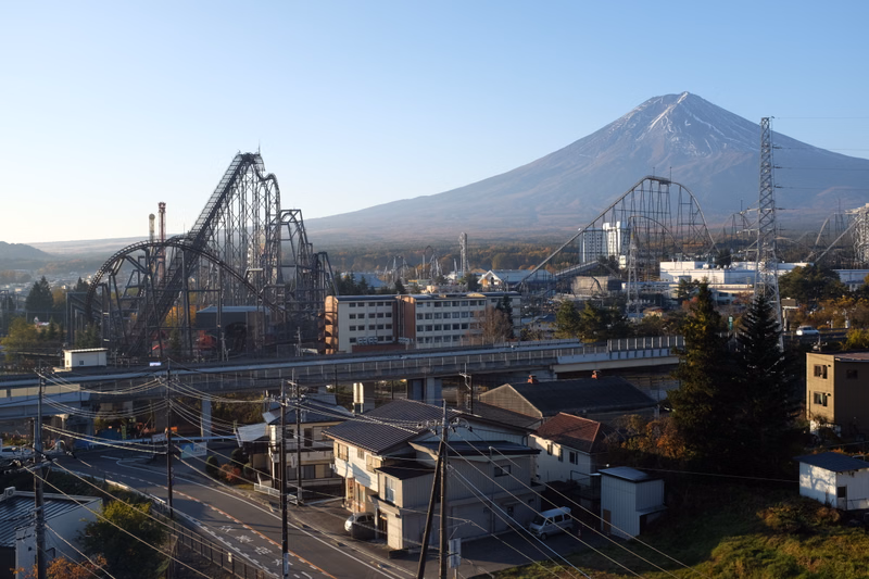 A large roller coaster dominates the foreground against the backdrop of a majestic, snow-capped mountain under a clear blue sky.