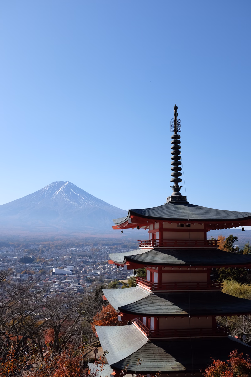 A traditional red temple structure overlooks a city with a large, snow-capped mountain in the background under a clear blue sky.