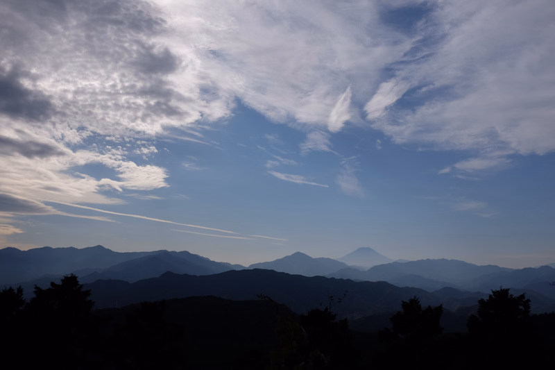 A wide view of layered mountains under a bright blue sky filled with scattered white clouds.