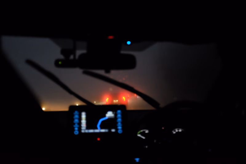 A nighttime view of a car interior with a map displayed on the dashboard and a rearview mirror.