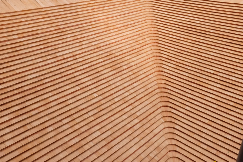 A close-up view of warm-toned wooden slats forming a curved, overlapping roof structure.
