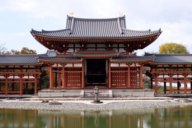 A large, traditional Japanese temple building with a dark tiled roof is situated on a small island surrounded by water.