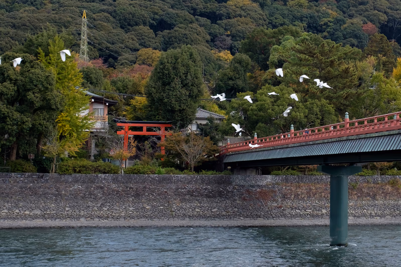 A serene seascape with a bridge and birds in flight, set against a backdrop of lush trees and a traditional Japanese torii gate.