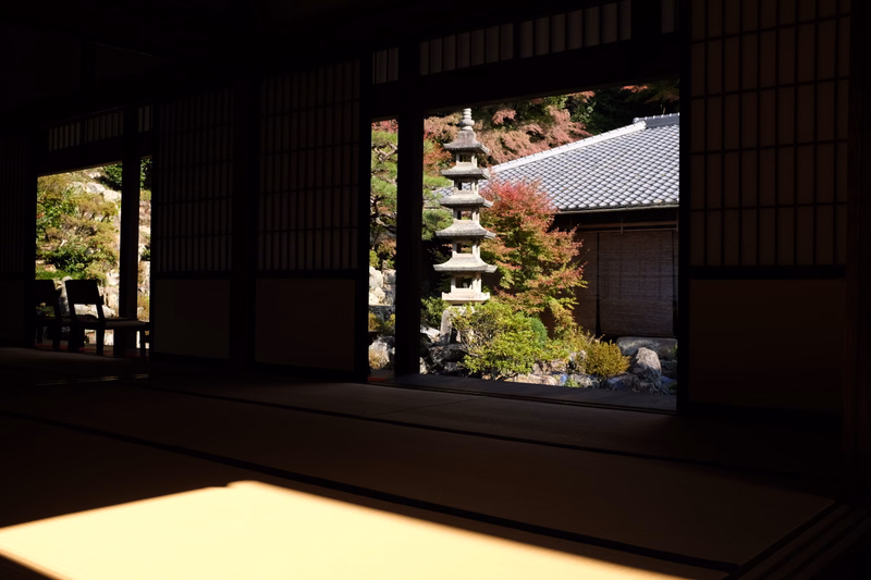 A view through dark wooden lattice doors into a traditional Japanese garden featuring a multi-tiered pagoda and tiled roof building.