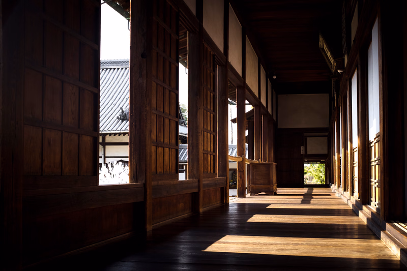 A long, dark wooden corridor with large windows lets shafts of sunlight illuminate the wooden floor.