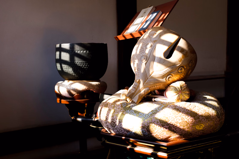A metallic, abstract sculpture rests on a patterned, round decorative object on a dark wooden table.