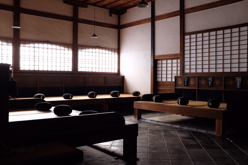 A traditional Japanese tatami room featuring wooden floors, sliding shoji screens, and low wooden platforms with futon bedding.
