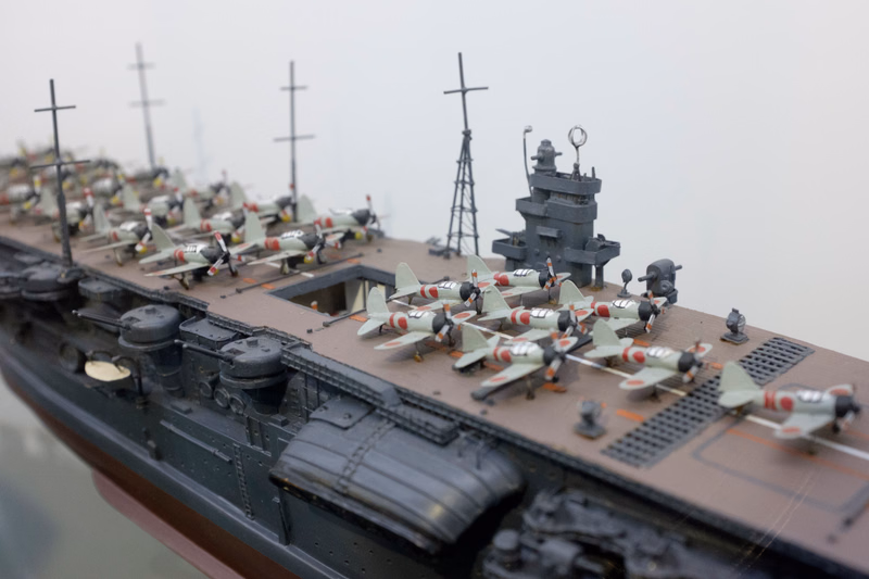 A detailed model of an aircraft carrier with numerous miniature airplanes parked on its flight deck under an overcast sky.