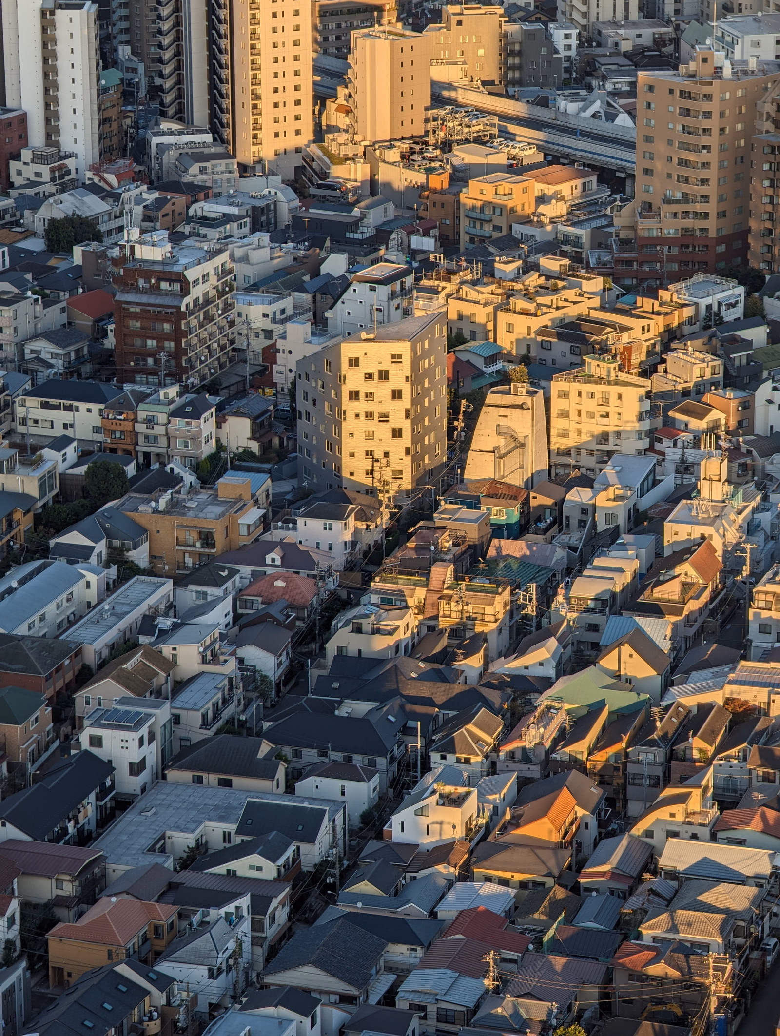 A dense urban cityscape view showing numerous residential buildings and rooftops under a bright sky.