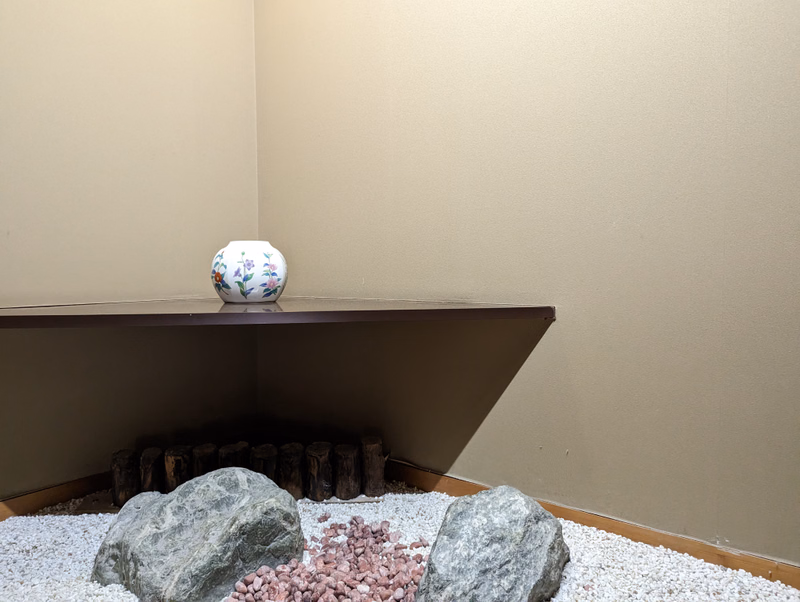A small decorative vase sits on a brown shelf above a display of large rocks and pink pebbles.