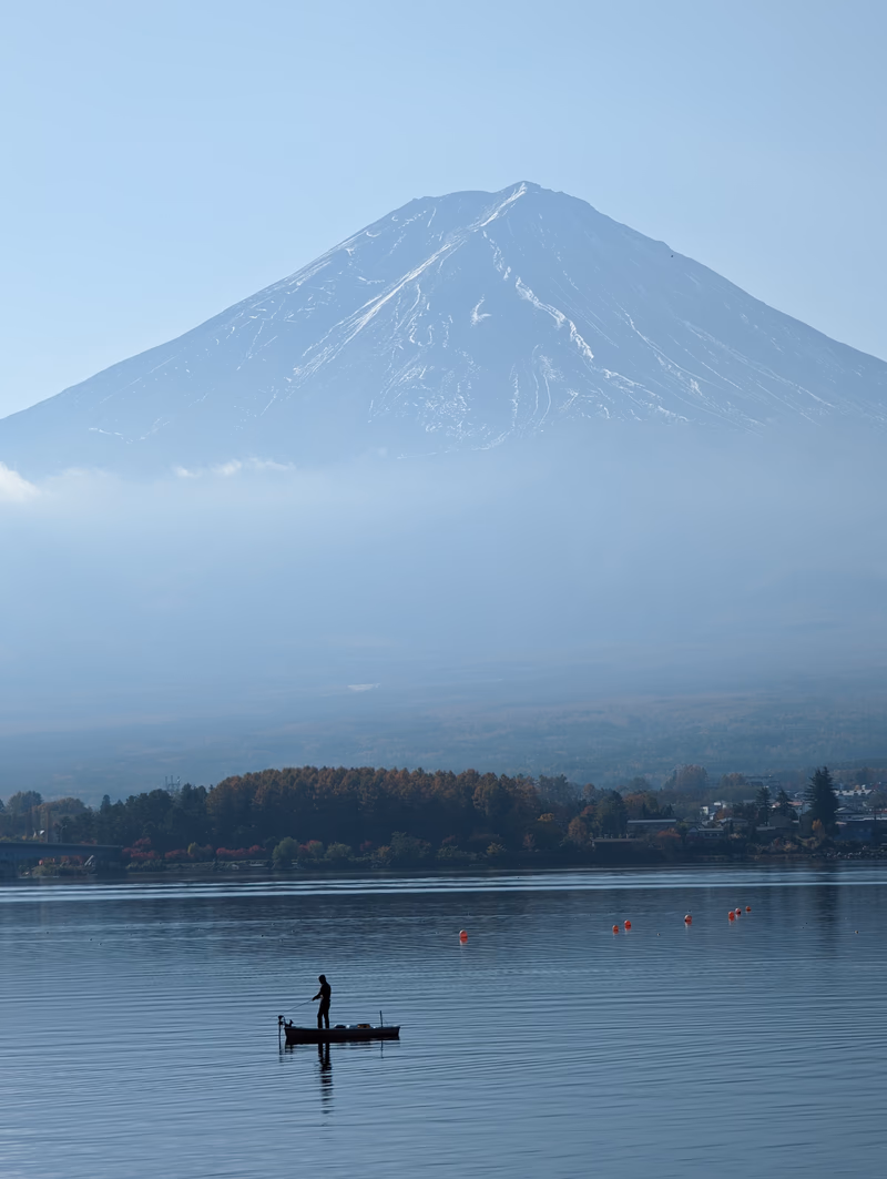 A serene lake with a lone fisherman and a majestic snow-capped mountain in the background.