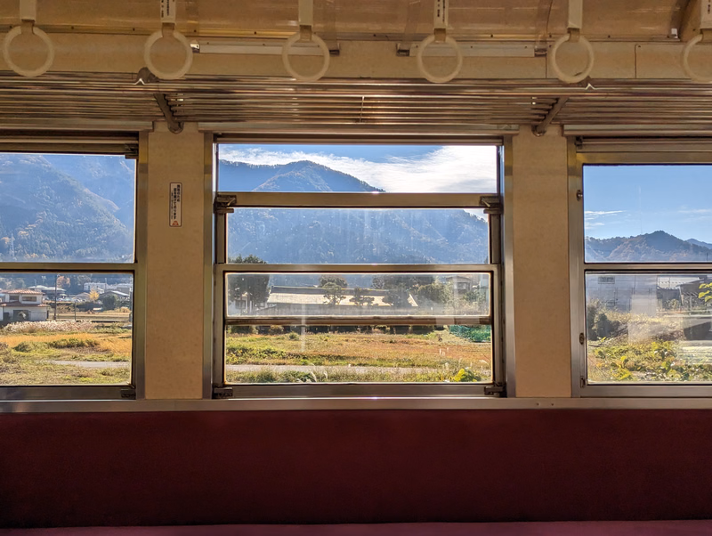 A view from a train window shows rolling hills and mountains under a bright sky.