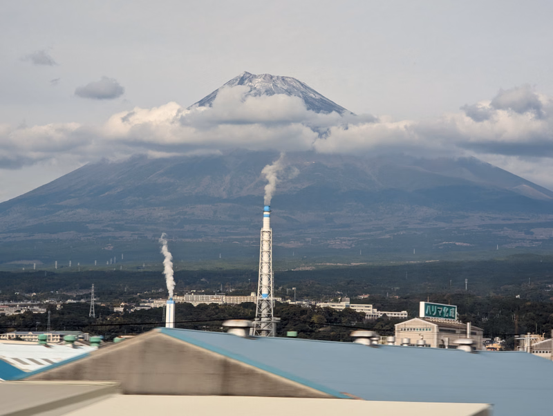 A large volcano is visible in the background, with smoke rising from a power plant in the foreground.