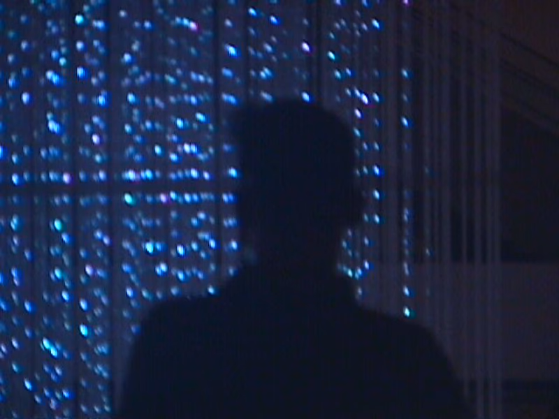 A silhouette of a person standing in front of a background of blue lights, creating a visually striking and atmospheric scene.
