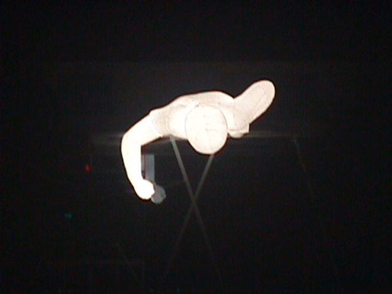 A person in a white wetsuit is diving or snorkeling in dark water, viewed from below.