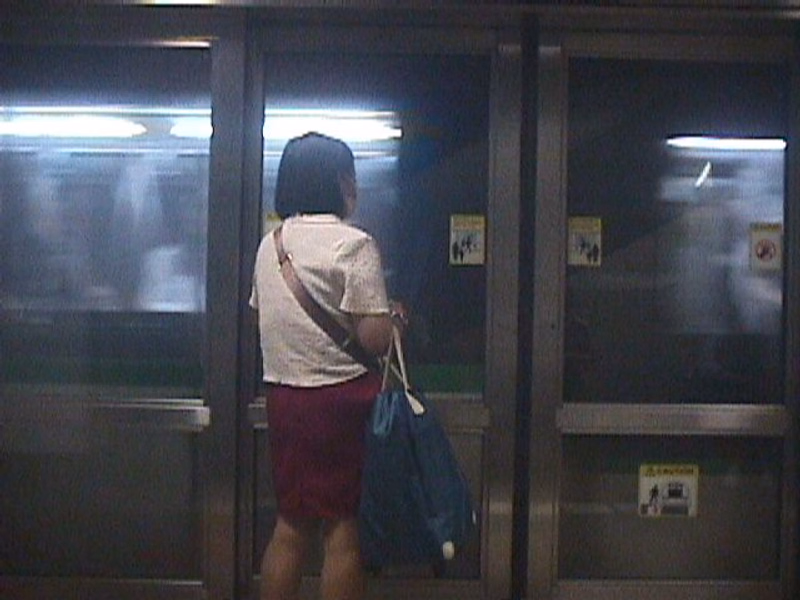 A person wearing a light-colored shirt and red shorts stands inside a modern train car.
