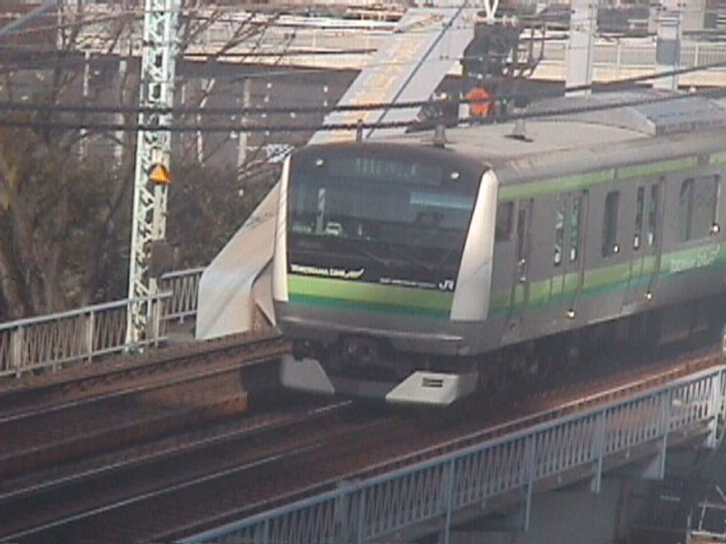 A modern green and white commuter train is visible on elevated railroad tracks in an urban setting.