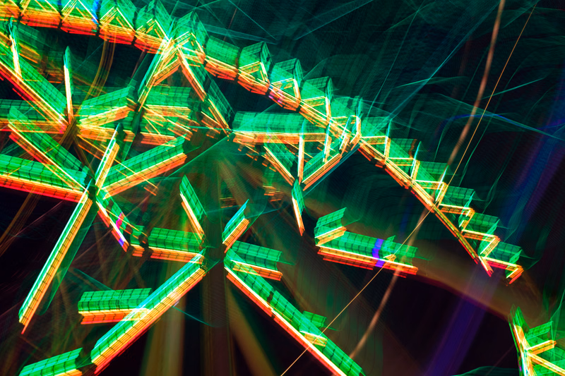 An abstract digital artwork featuring bright green and red geometric shapes interwoven with glowing lines and patterns against a dark background.