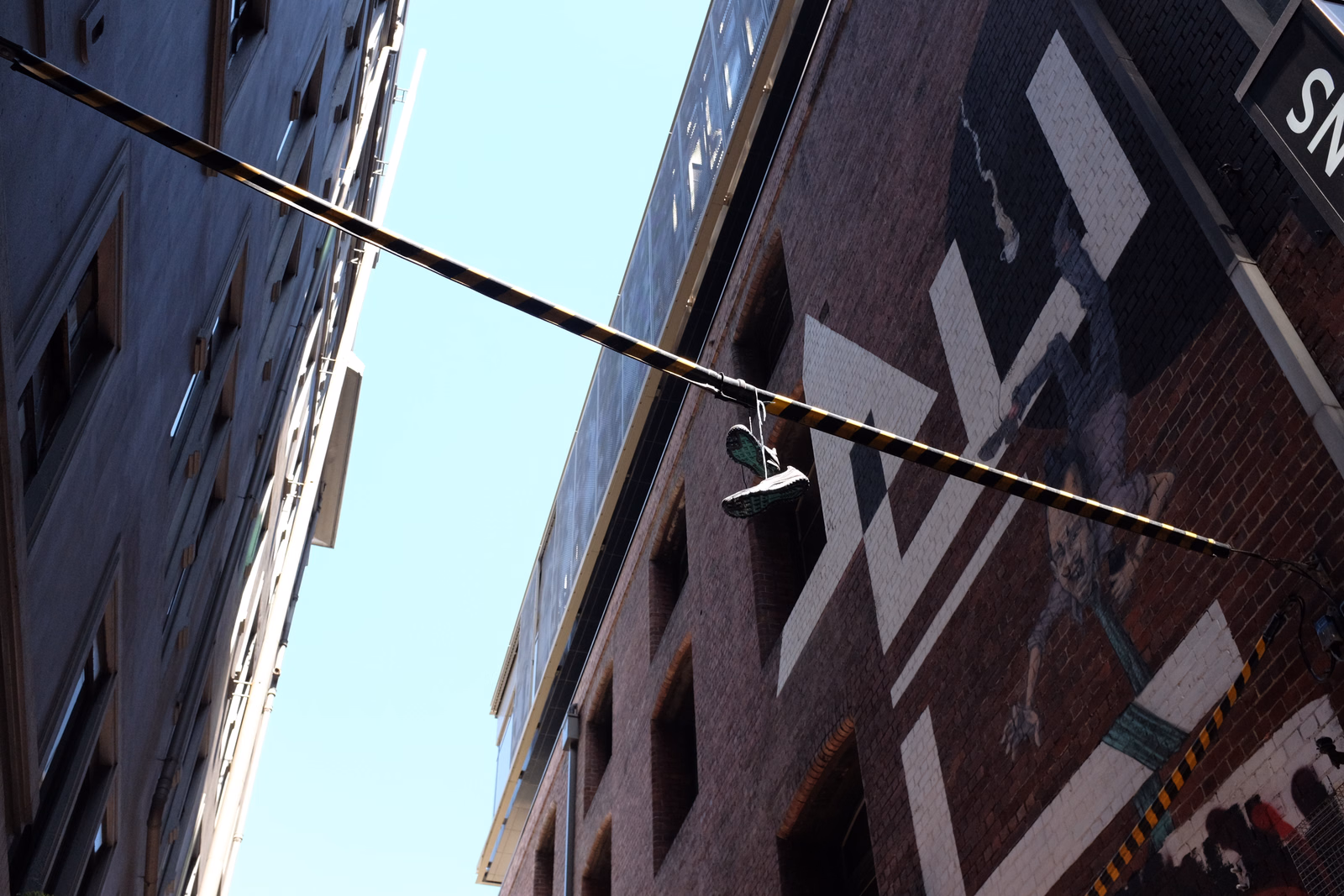 A long metal rod stretches across the frame, passing in front of a building covered in large white graffiti, with the text "SN" visible on the right.