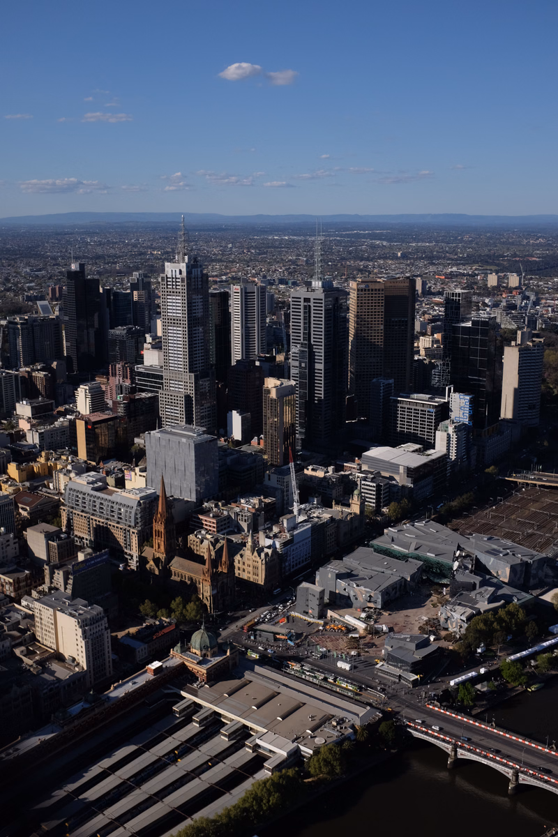 A high-angle panoramic view of a dense city skyline featuring numerous modern and older buildings alongside a river and train station.