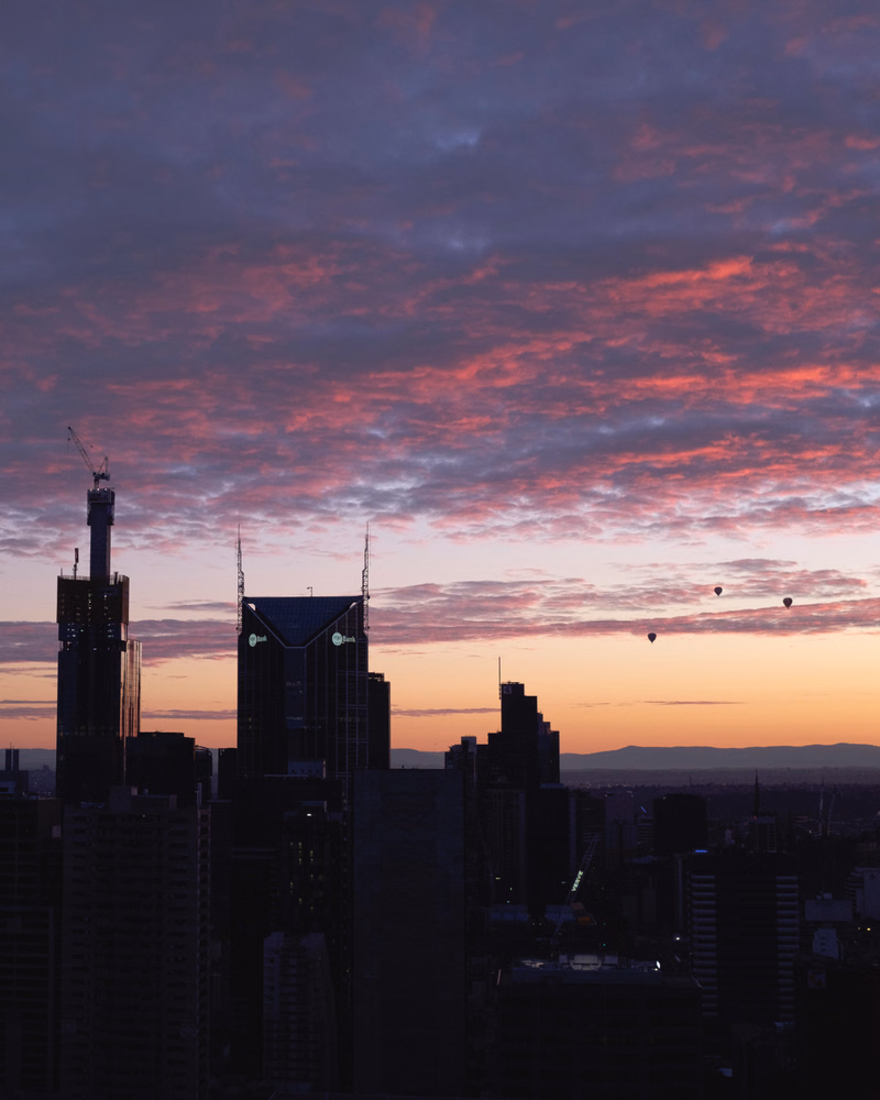 A nighttime cityscape silhouette against a dramatic sky filled with pink and purple clouds during sunset.