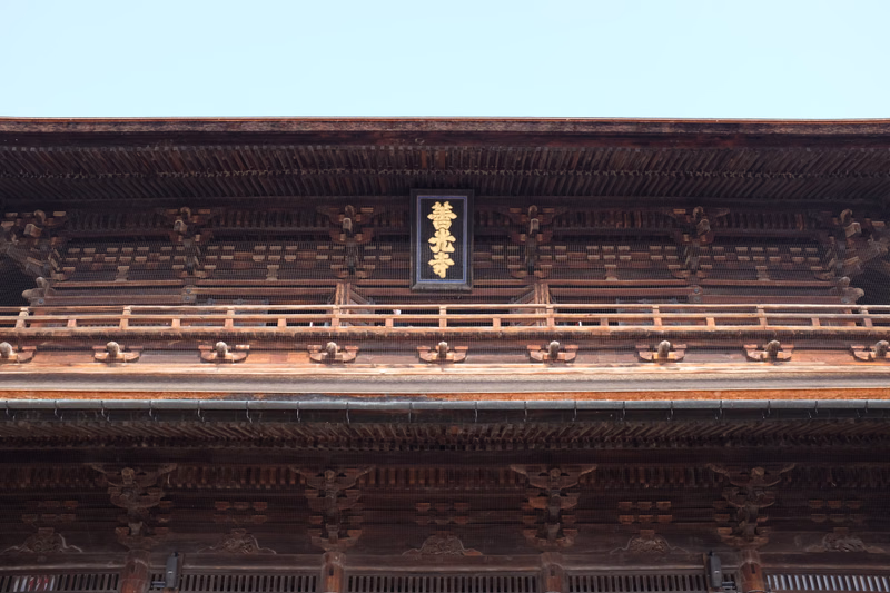 A close-up view of traditional Japanese temple architecture featuring intricate dark wood carvings and a plaque with Japanese characters.