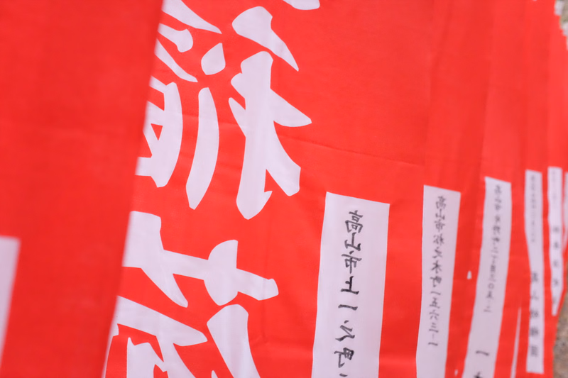 A close-up of a bright red banner featuring large white Japanese characters, with smaller text visible that reads "百日市村一九六三".