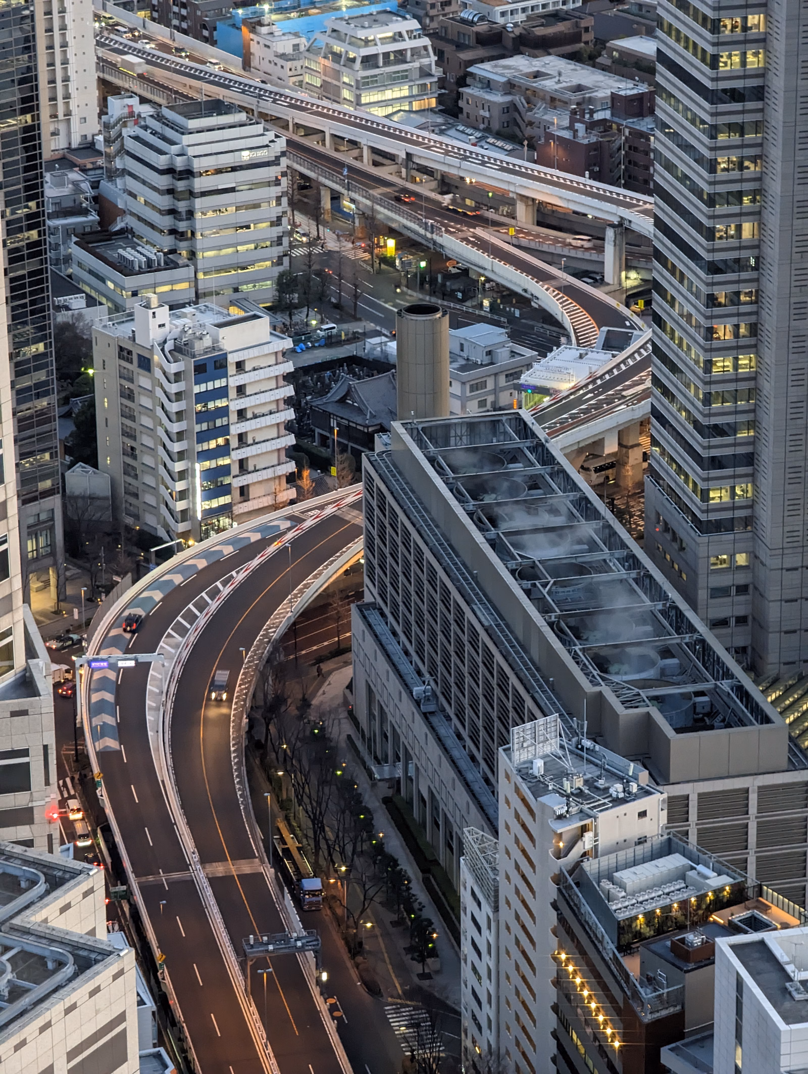 An aerial view of a dense cityscape featuring multiple elevated highways and numerous modern buildings at night.