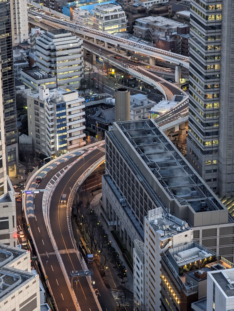 An aerial view of a dense cityscape featuring multiple elevated highways and numerous modern buildings at night.