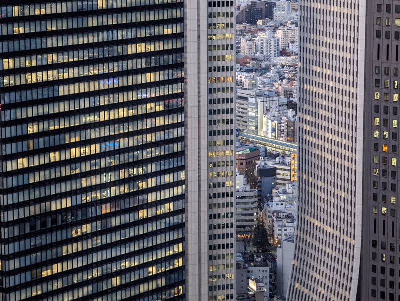 A view of modern skyscrapers in a dense city, showing illuminated windows in the buildings.