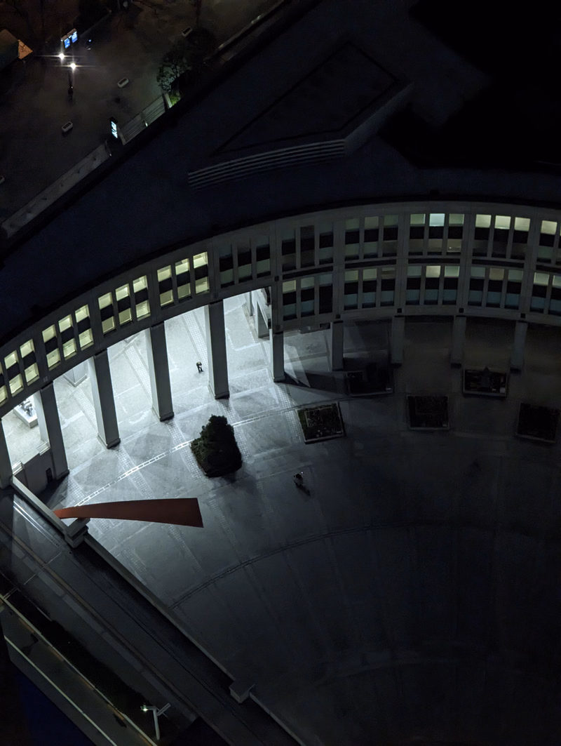 A nighttime aerial view of a modern building with a curved facade featuring many illuminated windows.