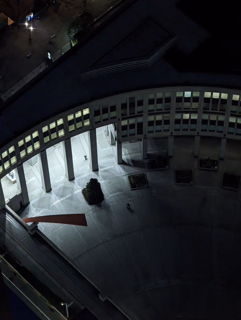 A night view of a modern architectural building with a person sitting on a chair inside.