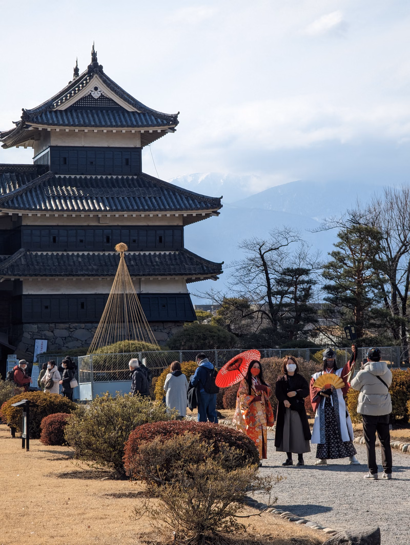 A traditional Japanese temple stands behind several people dressed in colorful kimonos in an outdoor setting.