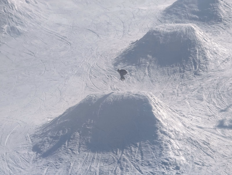 An aerial view shows several snow-covered volcanic cones in a mountainous, icy landscape.