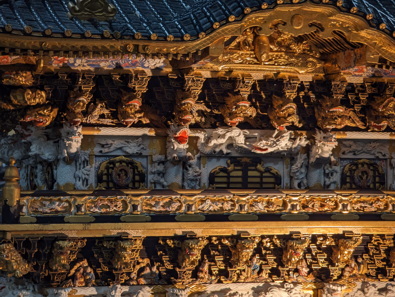 A close-up of a traditional Japanese wooden structure, adorned with intricate carvings and sculptures, featuring gold leaf and vibrant colors.