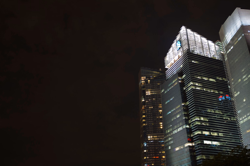 A nighttime cityscape featuring several modern skyscrapers illuminated against a dark sky.