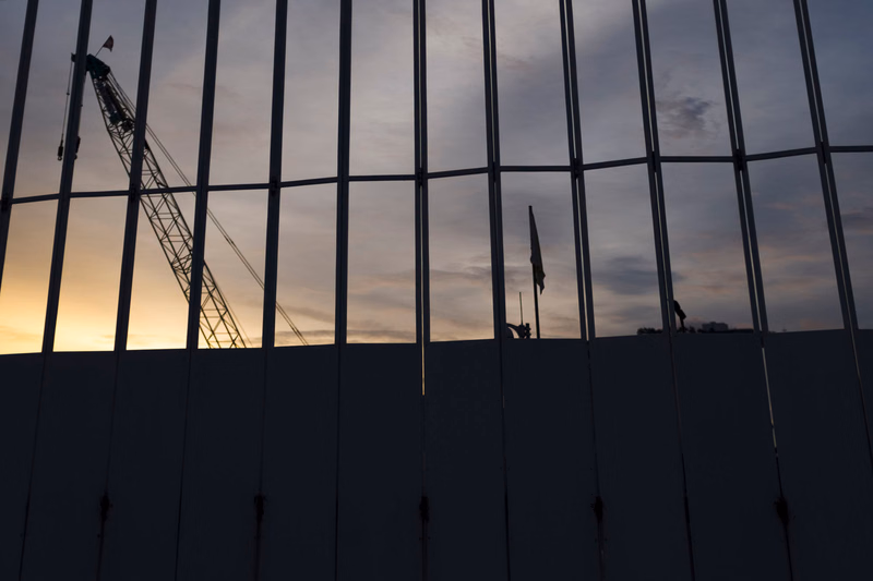 A construction crane is visible against a cloudy sunset through the glass facade of a modern building.