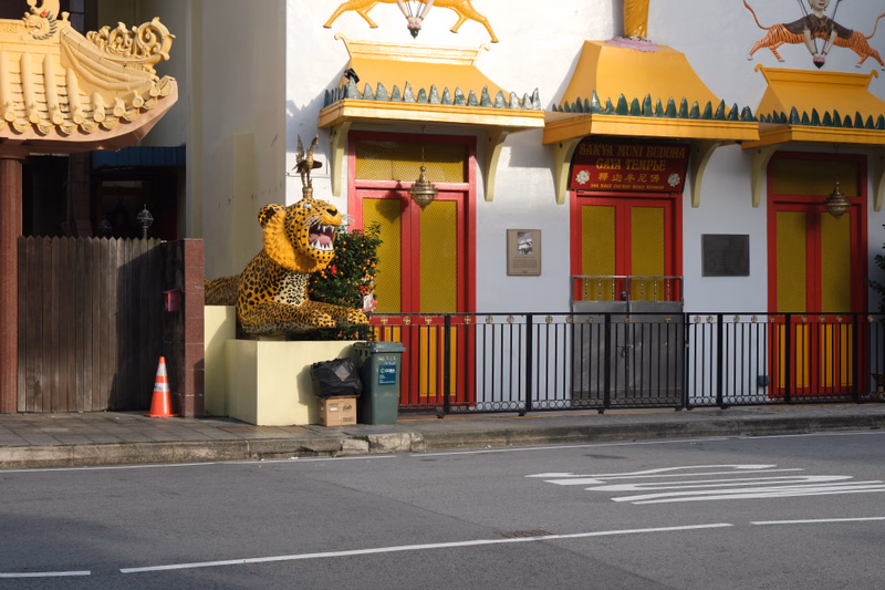 A colorful temple building features a large golden lion statue and a leopard statue near the entrance on a city street.