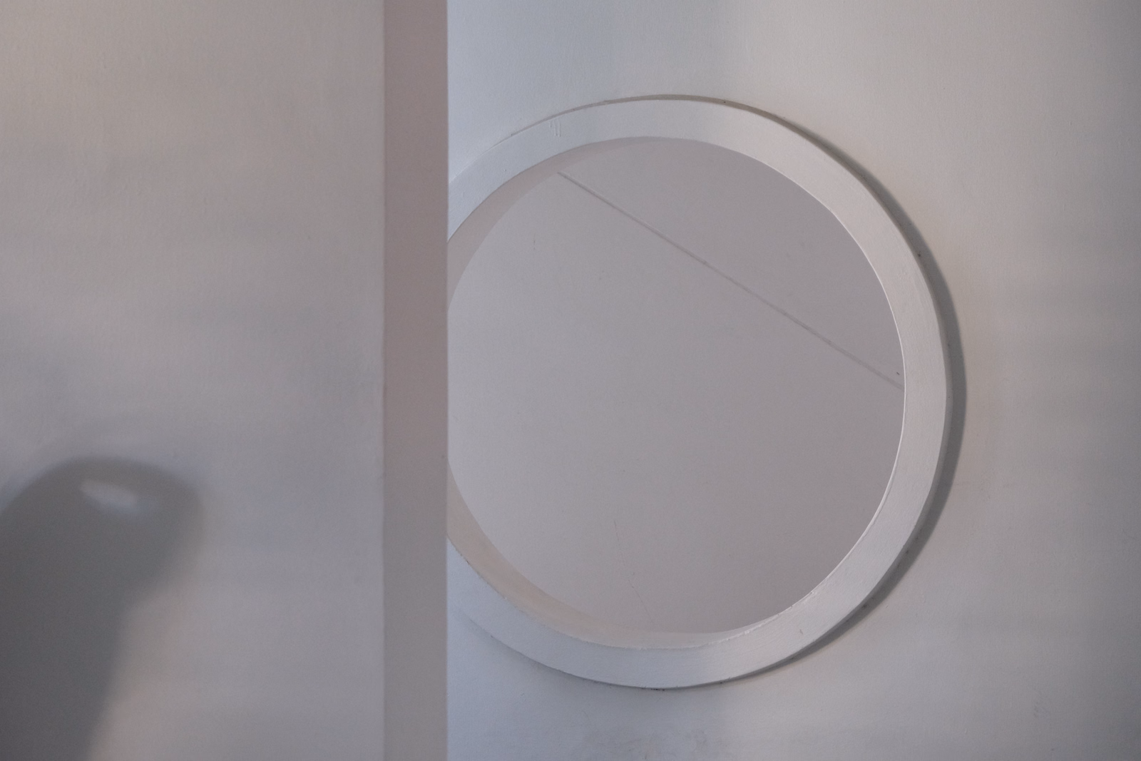 A large, circular mirror with a white frame is mounted on a plain white wall.