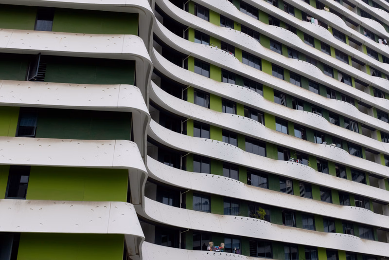A modern, curved apartment building features multiple stacked balconies with a distinctive white and green facade.