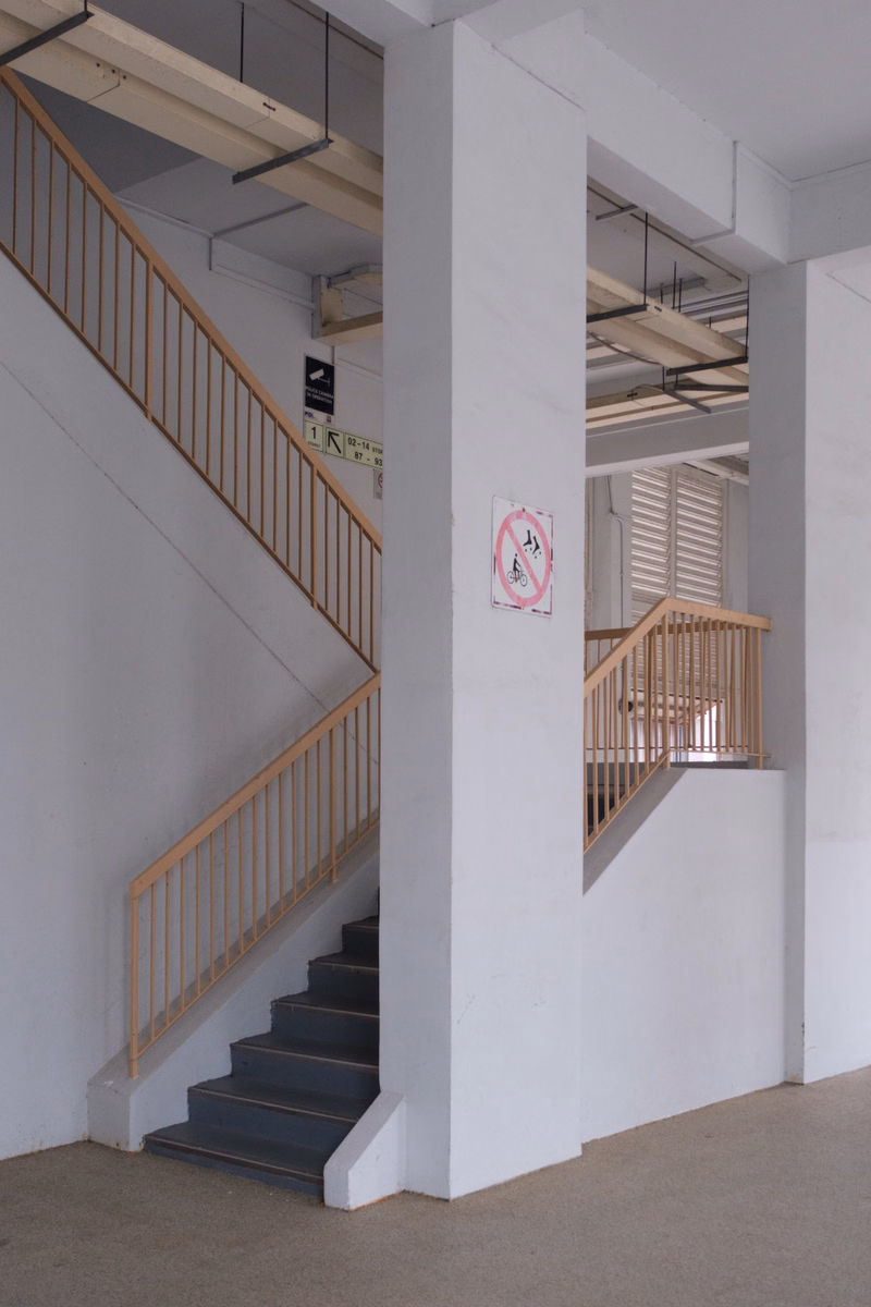 An interior view of a modern building featuring a wooden staircase with a railing, next to a white pillar with a 'No Smoking' sign.