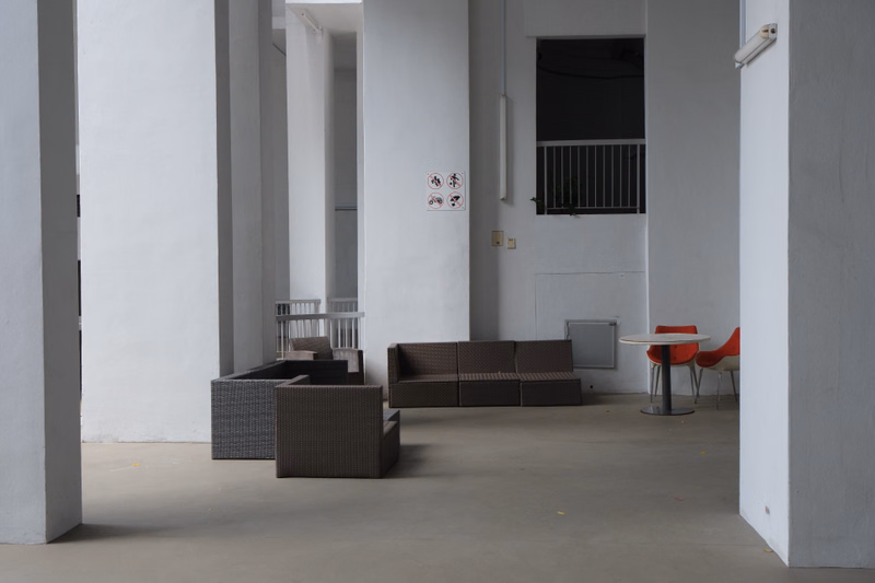 An outdoor patio area features various lounge furniture sets and a small red table against a white building exterior.